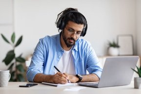Apotec Schulung Man mit blauem Hemd und Kopfhörern sitzt am Laptop und schreibt sich etwas auf