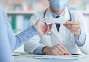 Ein Doktor in einem Kittel, der einer anderen Person einen Zettel überreicht.