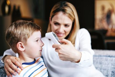 Stirnthermometer Eine Mutter, die ihrem Kind an der Stirn mit einem Stirnthermometer die Temperatur misst.