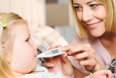 Fieberthermometer Ein Kind, das im Bett liegt, und eine Frau, die ihr mit dem Fieberthermometer im Mund misst.