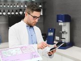 apotec Homepage Ein Apotheker mit einer Brille hält ein iPad mit der Hand fest und schaut auf das iPad.