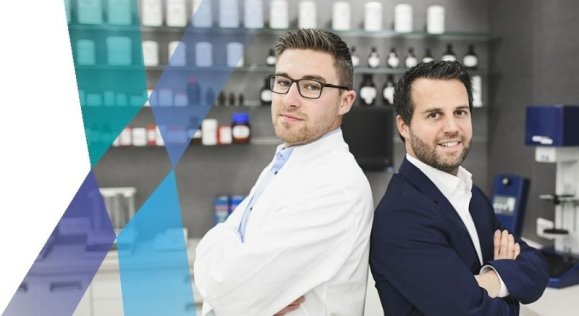 apotec_LabXpert_Teaser Ein Apotheker und ein Mann im Anzug stehen Rücken an Rücken, halten die Arme verschränkt und schauen in die Kamera.