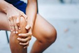 Schmerzendes Knie Eine Frau hält Ihr schmerzendes Knie zu