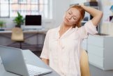 Wärmepflaster Verspannung Eine Frau sitzt vor dem Laptop und dehnt den Nacken